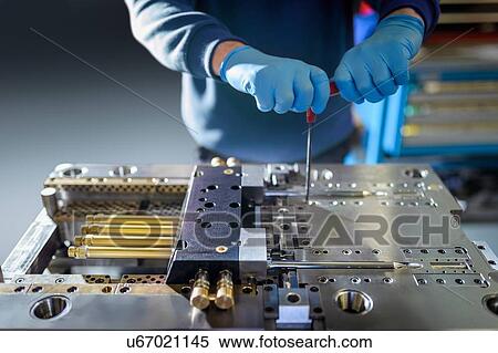 Stock Photography - Engineer working on plastic injection mould in precision engineering factory, mid section, close up. Fotosearch