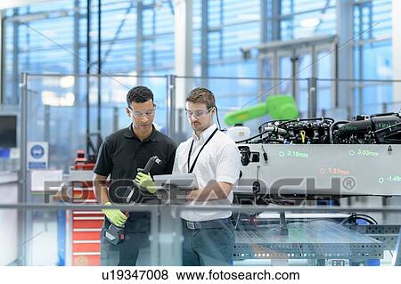 Stock Photo - Engineers with digital tablet and robot inspecting car in robotics research facility. Fotosearch