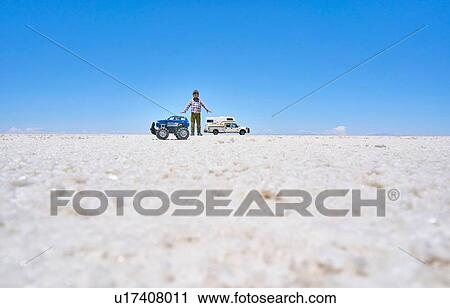 Stock Image - False perspective image of boy and toy truck on salt flats, standing taller than recreational vehicle in background, Salar de Uyuni, Uyuni, Oruro, Bolivia, South America. Fotosearch