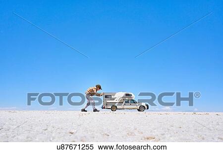Stock Photography - False perspective image of boy on salt flats, pretending to push recreational vehicle, vehicle in background, Salar de Uyuni, Uyuni, Oruro, Bolivia, South America. Fotosearch