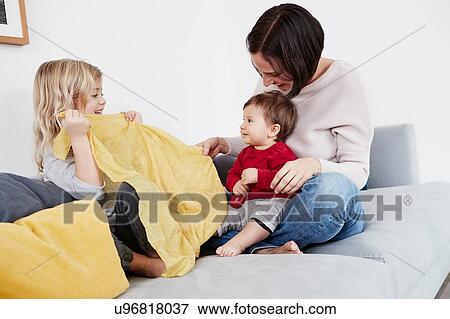 Family sitting on sofa, young girl playing peek-a-boo with baby sister View Large Photo Image Stock Photo - Family sitting on sofa, young girl playing peek-a-boo with baby sister. Fotosearch