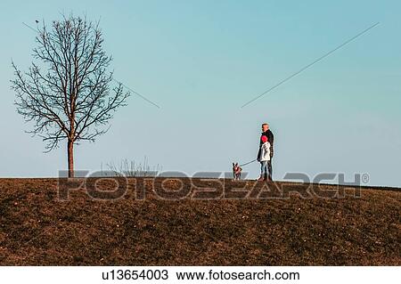 Stock Image - Father and daughter walking dog on hillside. Fotosearch