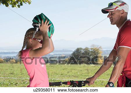 Father watching girl cyclist putting on bicycle helmet View Large Photo Image Stock Image - Father watching girl cyclist putting on bicycle helmet. Fotosearch