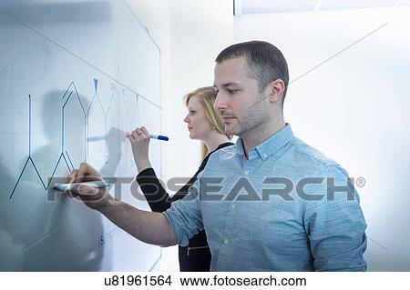 Picture - Female and male scientists drawing on white board in meeting room. Fotosearch