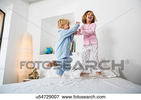 Stock Photo - Female and male twins jumping together on bed. Fotosearch