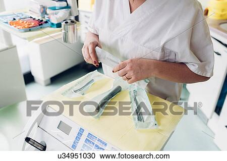 Stock Image - Female dentist in dentist office, preparing dentistry equipment, mid section. Fotosearch
