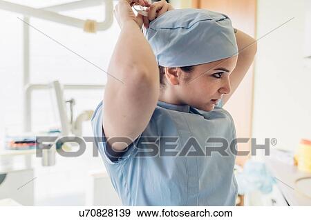 Stock Photo - Female dentist in dentist office, putting on surgical cap. Fotosearch