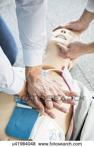 Stock Photo - First-aiders practising CPR on training dummy. Automated external defibrillator pads have been placed on the dummy's chest.. Fotosearch