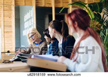 Four businesswomen sitting at desk, looking at documents View Large Photo Image Stock Photo - Four businesswomen sitting at desk, looking at documents. Fotosearch