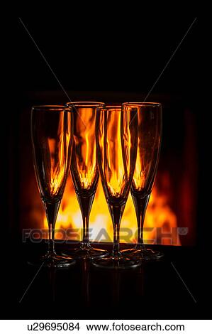 Picture - Four champagne glasses on table in front of burning fire. Fotosearch