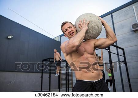 Four people exercising in gymnasium, man in foreground using atlas stone View Large Photo Image Picture - Four people exercising in gymnasium, man in foreground using atlas stone. Fotosearch