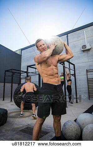 Stock Photo - Four people exercising in gymnasium, man in foreground using atlas stone. Fotosearch