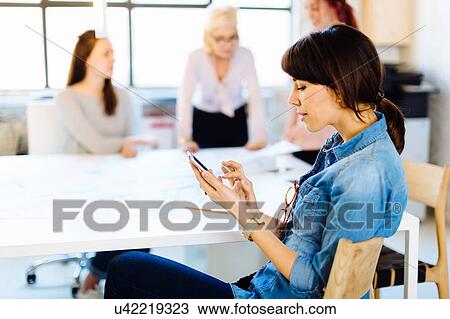 Four women in business meeting, woman in foreground using smartphone View Large Photo Image Stock Image - Four women in business meeting, woman in foreground using smartphone. Fotosearch