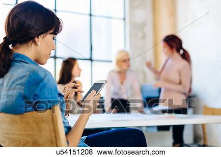 Stock Photo - Four women in business meeting, woman in foreground using smartphone. Fotosearch