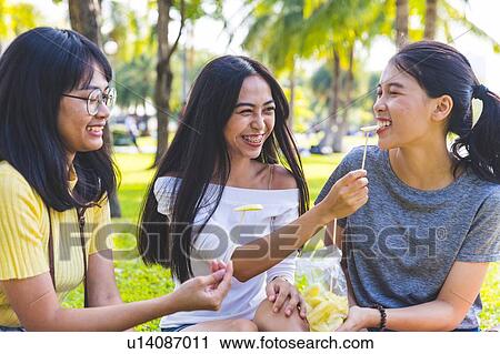 Stock Image - Friends enjoying snacks in park, Bangkok, Thailand. Fotosearch