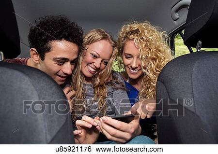 Friends in back seat of car looking at smartphone View Large Photo Image Stock Photograph - Friends in back seat of car looking at smartphone. Fotosearch