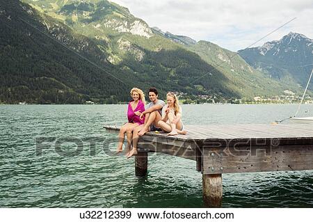 Stock Photo - Friends sitting together on edge of pier, Innsbruck, Tirol, Austria, Europe. Fotosearch