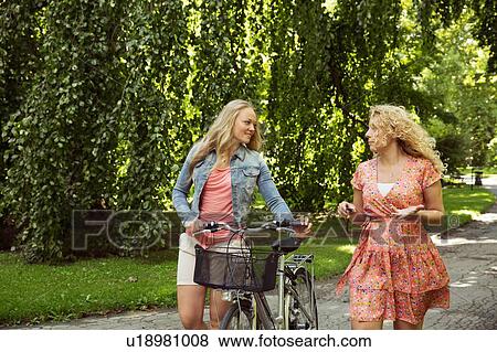 Stock Photo - Friends walking with bicycles chatting. Fotosearch