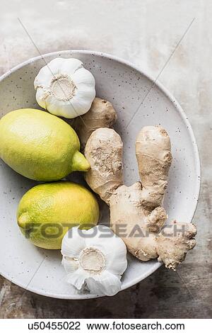 Stock Image - Ginger roots with lemon and garlic in ceramic bowl. Fotosearch