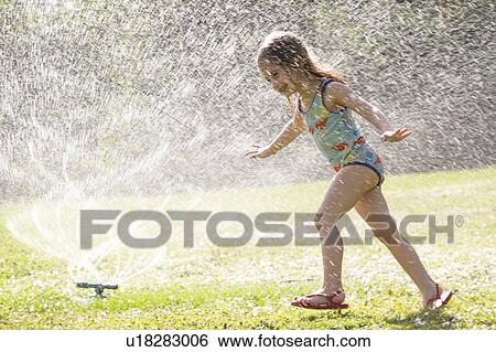 Stock Photograph - Girl (4-5) splashing in sprinkler water on lawn. Fotosearch