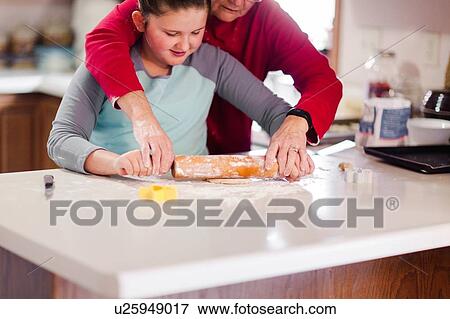 Stock Photo - Girl and grandmother rolling cookie dough together at kitchen counter. Fotosearch