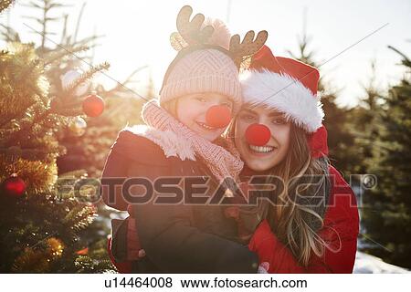 Stock Photo - Girl and mother in christmas tree forest with red noses, portrait. Fotosearch
