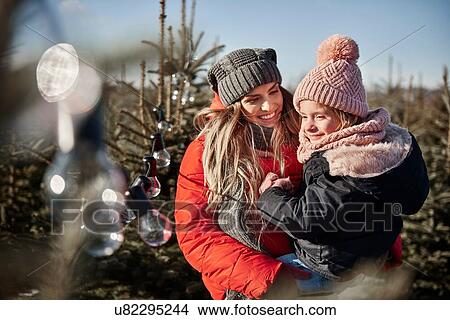 Picture - Girl and mother looking at forest christmas tree lights. Fotosearch