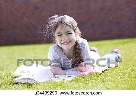 Stock Image - Girl lying on grass reading.. Fotosearch