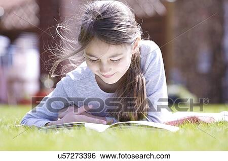 Stock Photograph - Girl lying on grass reading.. Fotosearch