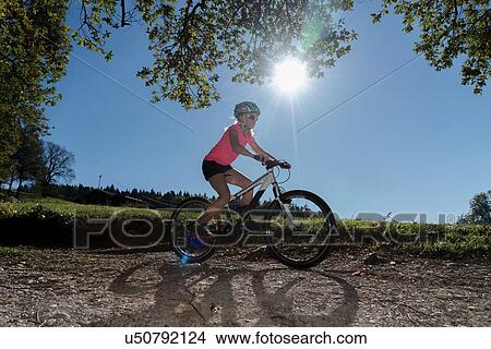Picture - Girl mountain biker cycling down sunlit dirt track. Fotosearch