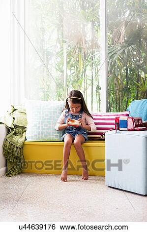 Stock Photograph - Girl on window seat looking at toy camera. Fotosearch