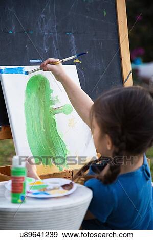 Stock Photo - Girl painting on canvas in garden, over shoulder view. Fotosearch