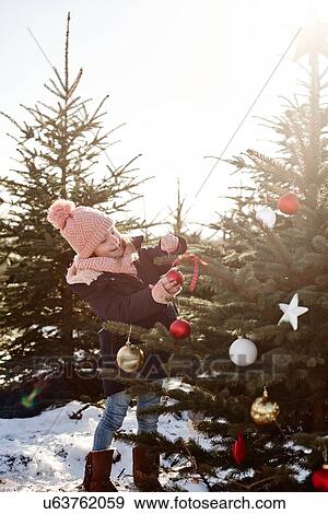 Stock Photo - Girl putting baubles onto forest christmas tree. Fotosearch