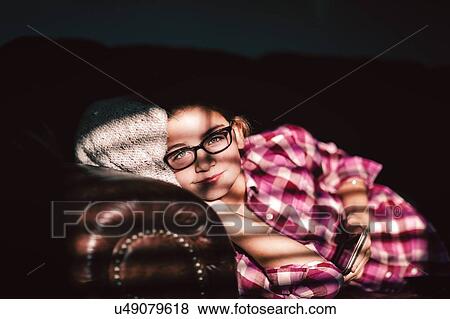 Stock Photo - Girl relaxing on sofa, holding smartphone. Fotosearch