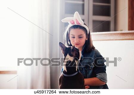 Girl sitting with dog, indoors, girl wearing Easter bunny ears View Large Photo Image Picture - Girl sitting with dog, indoors, girl wearing Easter bunny ears. Fotosearch