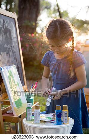 Stock Image - Girl squeezing paint onto palette in garden. Fotosearch