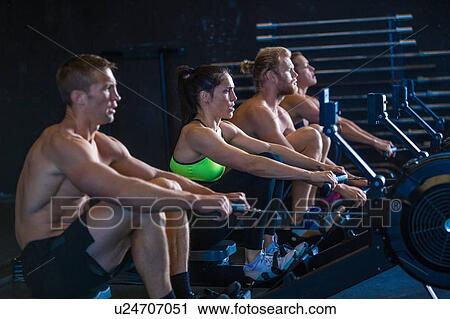 Stock Image - Group of people exercising in gymnasium, using rowing machines. Fotosearch