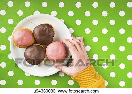 Stock Image - Hand picking donut with sweet strawberry topping.. Fotosearch