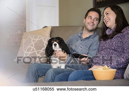 Stock Photography - Happy mid adult couple relaxing on sofa with dog. Fotosearch