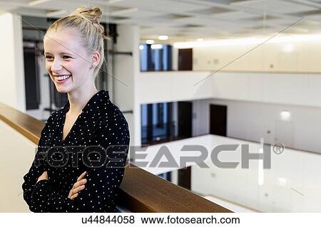 Stock Photo - Happy young businesswoman with arms folded in office atrium. Fotosearch