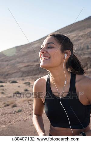 Stock Image - Happy young female runner listening to earphones in arid landscape. Fotosearch