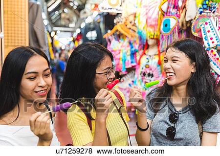 Stock Photo - Happy young women with ice lollies in bazaar, Bangkok, Thailand. Fotosearch
