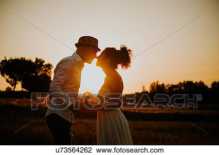 Stock Image - Heterosexual couple in field at sunset, holding hands, face to face. Fotosearch