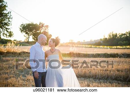 Stock Image - Heterosexual couple standing in field, face to face, smiling. Fotosearch