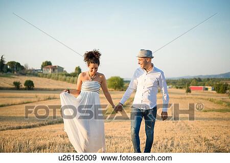 Stock Photo - Heterosexual couple walking through field, holding hands, smiling. Fotosearch