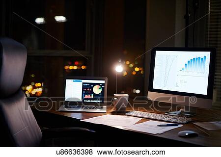 Stock Photo - Laptop and computer on office desk at night. Fotosearch