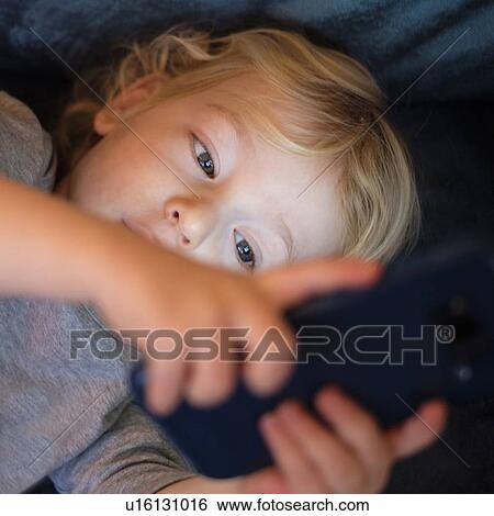Stock Photograph - Little boy (2-3) lying down and playing game on smart phone. Fotosearch
