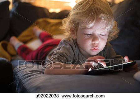 Stock Photo - Little boy (2-3) lying on front and playing game on smart phone. Fotosearch