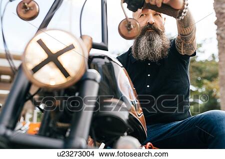 Picture - Low angle view of mature male hipster astride motorcycle. Fotosearch