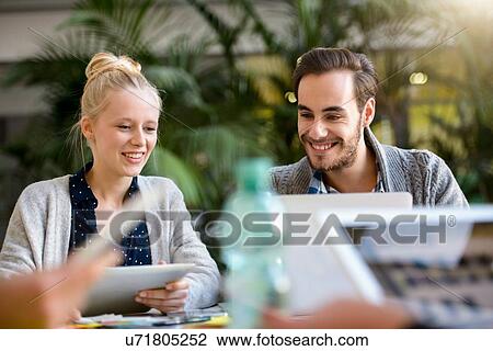 Stock Image - Male and female designer looking at laptop on design studio desk. Fotosearch